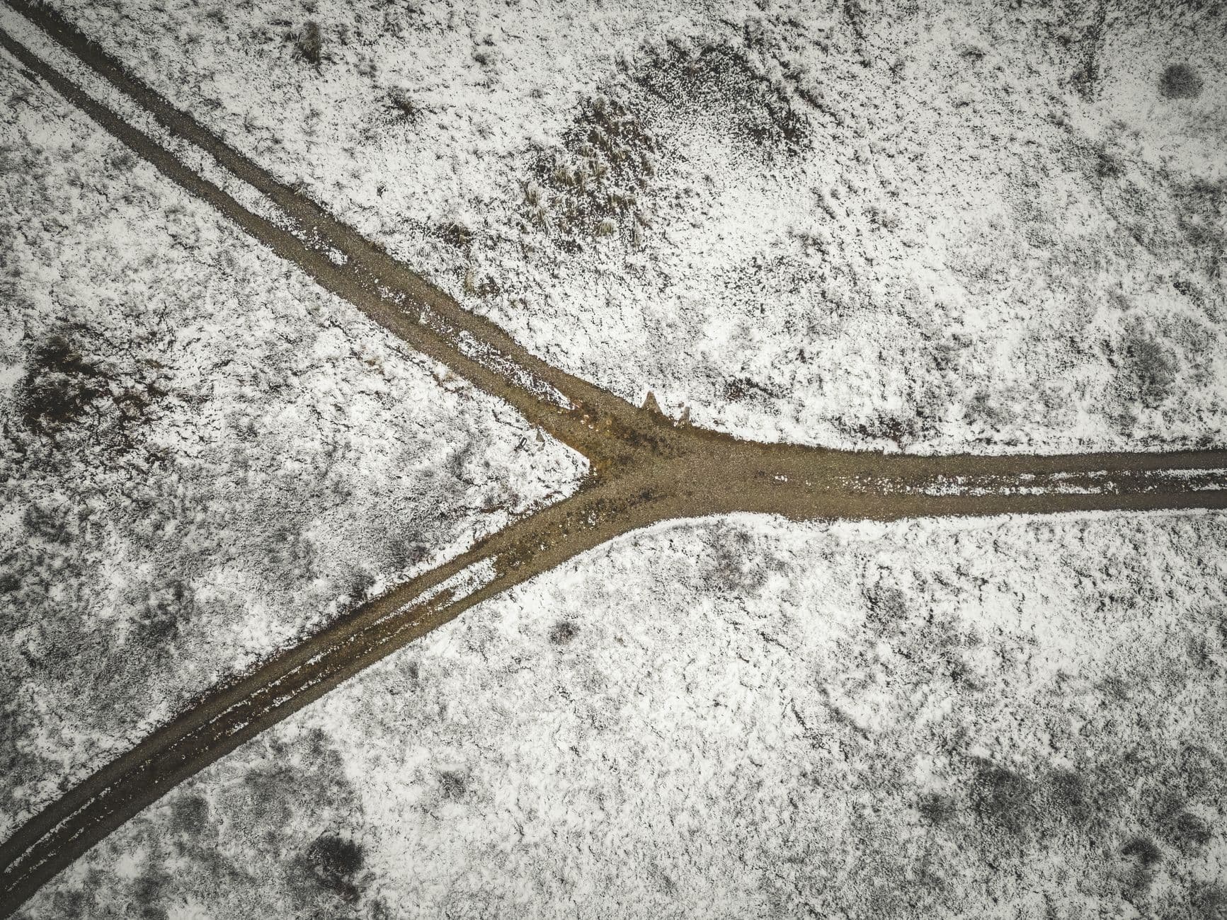 Grusvei som deler seg i to, sett rett ovenfra i snødekt landskap