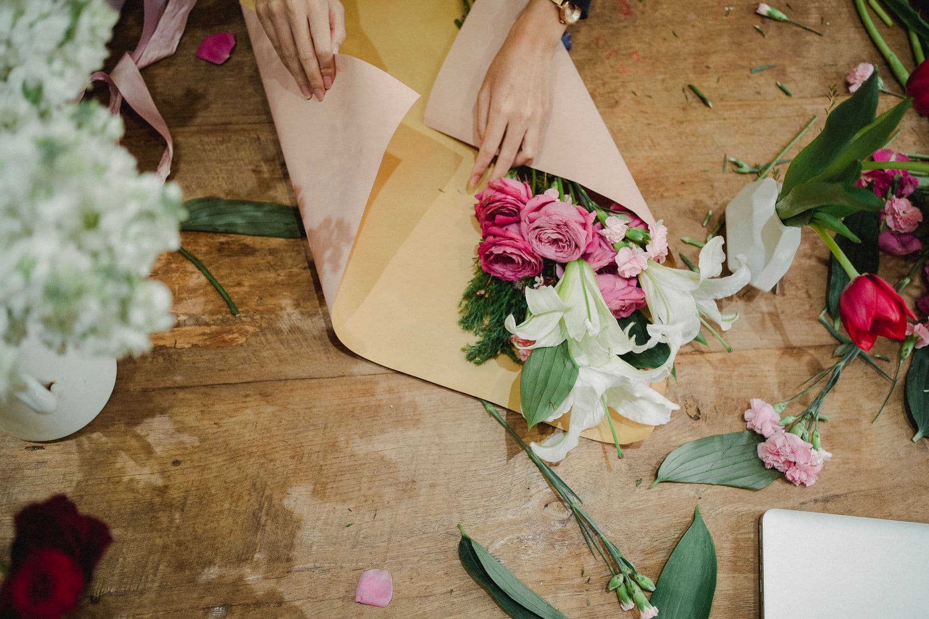 Blomsterbinder pakker bukett i kraftpapir på arbeidsbord, sett ovenfra